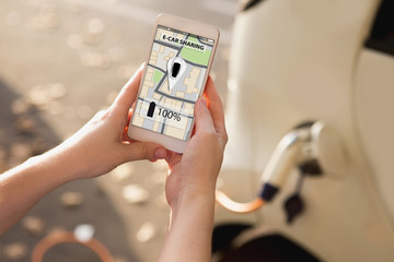 Hand with phone on a background of electric cars charging point. E-car sharing concept