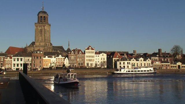 Deventer Hanseatic town on the river IJssel, passenger ferry sailing on camera.  St. Lebuins Church towering above the historic houses on the quay. DEVENTER, THE NETHERLANDS - December 2015