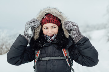 Smiling woman dressed warm holding her hood with snowy gloves.