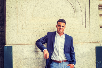 Happy African American Man in New York. Wearing blue blazer, white shirt, a black college student standing against vintage wall on campus, smiling. Instagram filtered effect..