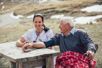 Nurse measuring old patient's blood pressure outdoor
