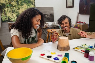Man assisting woman in painting vase
