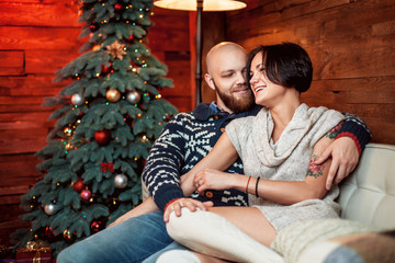 Beautiful couple sitting on the couch embrace in a decorated festive interior with a Christmas tree. The concept of a family celebration, new year's eve