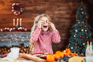 Happy little child, cute kid girl at the table in domestic kitchen making gingerbread xmas cookies decorated for Christmas holiday. Girl helping and having fun