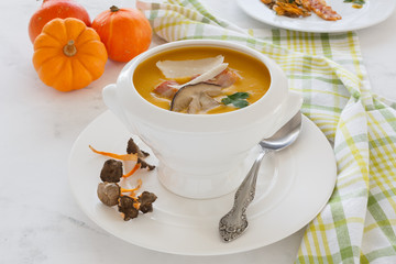 cream soup from vegetables of a pumpkin, a leek, carrots with a Parmesan, a white mushroom and bacon, a parsley in a white soup plate. still life covered table view from above.