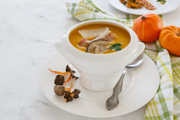 cream soup from vegetables of a pumpkin, a leek, carrots with a Parmesan, a white mushroom and bacon, a parsley in a white soup plate. still life covered table view from above.