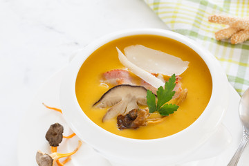 cream soup from vegetables of a pumpkin, a leek, carrots with a Parmesan, a white mushroom and bacon, a parsley in a white soup plate. still life covered table view from above.