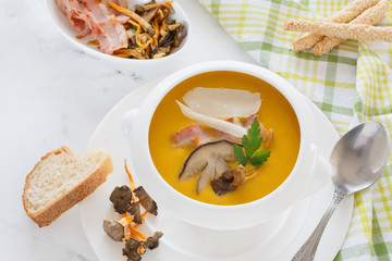 cream soup from vegetables of a pumpkin, a leek, carrots with a Parmesan, a white mushroom and bacon, a parsley in a white soup plate. still life covered table view from above.