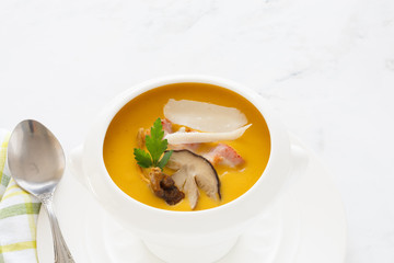 cream soup of pumpkin vegetables, leeks, carrots with Parmesan, white mushroom and bacon in a white soup plate. still life covered table view from above.
