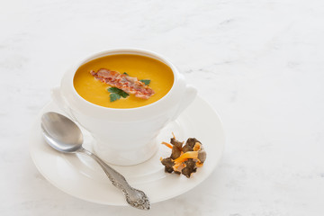 cream soup from vegetables pumpkin, leeks, carrots with Parmesan, mushroom and bacon, parsley in a white soup plate. still life covered table view from above.