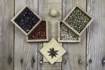 Several peppers, juniper and star anise on small wooden square bowls
