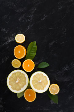 oranges, lime, lemon with green leaves on a black textural background top view. still life with citrus on a dark background.