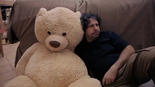 A sad depressed man seeking comfort and a hug from his toy friend, a giant teddybear.
