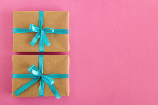 Two gift boxes wrapped of craft paper and blue ribbon on the pink background, top view.