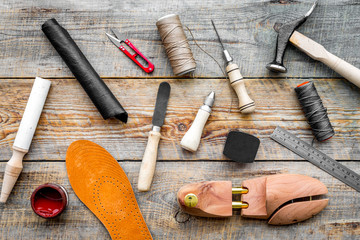 Shoe repair. Wooden last, hammer, awl, knife, thread on wooden background top view