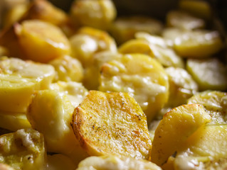 Raw potatoes prepared for baking with flavorings and cheese on tray.