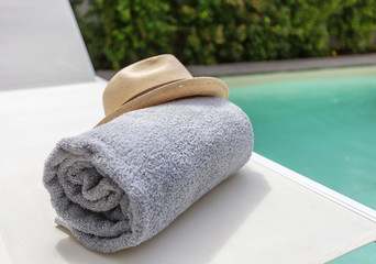 Plakat Straw hat on the sun lounger and a towel by the pool. Vacation with a tourist.