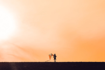  boy launching a kite. silhouette of a child with a kite in hands on a sunset background. Happy time of childhood. the wind of change. The concept of future. Copy space for your text
