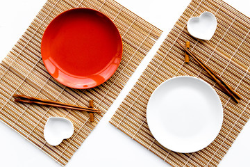 Table setting for sushi roll. Empty plate on mat near chopstick and bowl for sause on white...