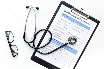 Health insurance for reception at the doctor. Document, stethoscope, pad, glasses on white background top view