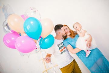 Fototapeta na wymiar a young family of three people, mom's dad and daughter's one year old stands inside the room. Holding a balloon in her hand, a woman with red long hair is holding a child in her arms . Birthday party