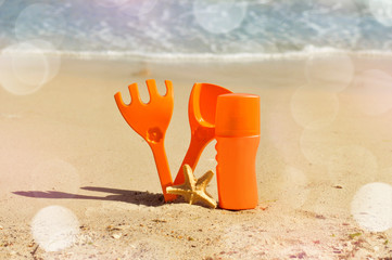 oil tanning spray on the shore in the sand with the children's spade and rake
