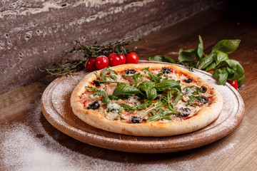 Tasty italian pizza with cherry tomato, ham and black olives on wooden table with herbs