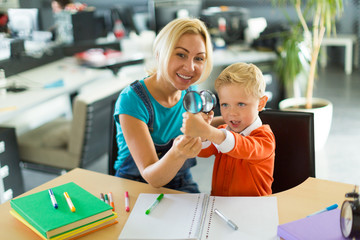 Cute boy and woman sit at the desk in the office and play