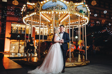 Couple on the carousel background. A beautiful pair of loving newlyweds gently embrace on the evening city background. © shchus
