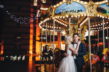 Couple on the carousel background. A pair of loving newlyweds gently embrace on the evening city background.