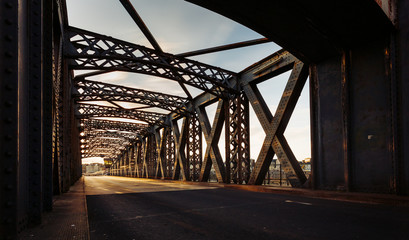 Asphalt road under the steel construction of a city bridge on a sunny day. Urban scene in the bridge tunnel. Long exposure. Toned