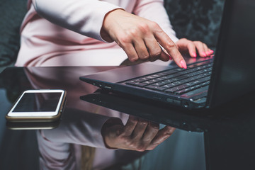 Typing on a laptop keyboard. Laptop and phone lying on the table. A woman is working on a computer, using a laptop. Work at home, in the room. Office at home. Business outline.