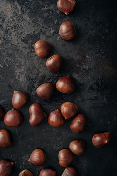 Sweet chestnuts on dark black rustic background. Pile of fresh chestnuts ready to roast shot over black antique background. Top view.