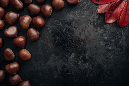Tasty chestnuts on dark black rustic background. Pile of fresh chestnuts ready to roast shot over black antique background. Top view, copy space.