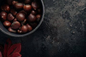 Tasty chestnuts on dark black rustic background. Pile of fresh chestnuts ready to roast in cast...