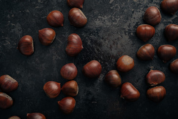 Fresh chestnuts on dark black rustic background. Pile of fresh chestnuts ready to roast shot over black antique background. Top view.