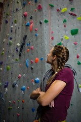 Athlete with rope looking up while standing by climbing wall in