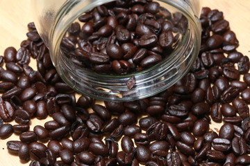 baked and roasted raw coffee beans with glass jar and white plastic scoop isolated on wood background.