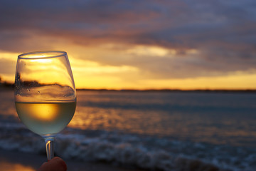 Female hand with a glass of white wine on the background of a beautiful sunset.  Travel vacations concept.