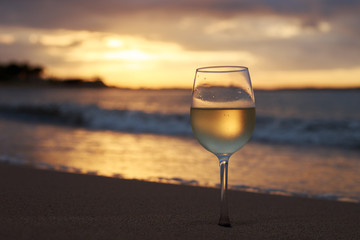 A glass  of white wine on the beach at sunset. Travel vacations concept.