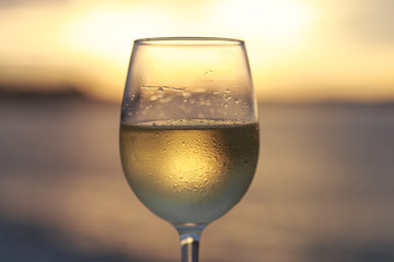 Wineglass of white wine at sunset dramatic sky background. Closeup. Travel vacations concept.