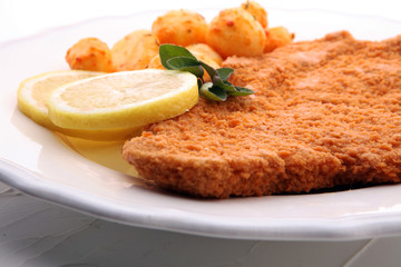 Golden schnitzel, boiled potatoes and lemon on a plate.