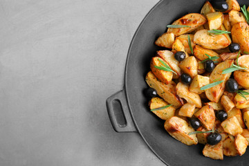 Delicious baked potatoes with rosemary and olives in pan on table