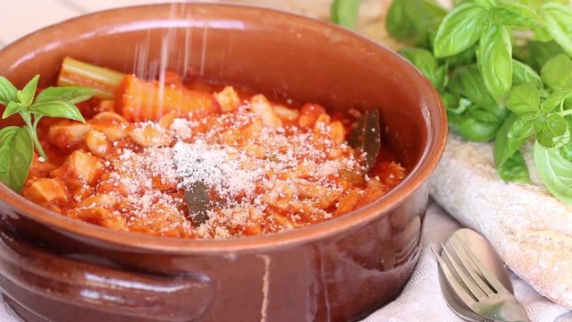 Grated Parmigiano cheese on a terracotta pot with tripe and beans.