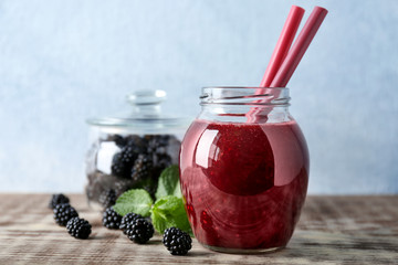 Delicious blackberry smoothie in glass jar on table against light background