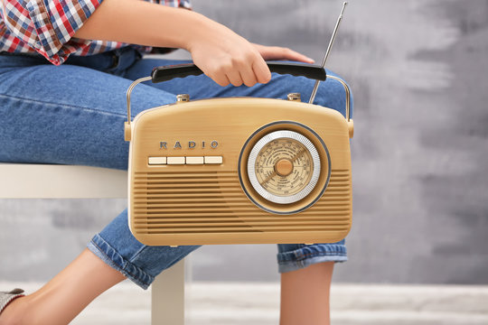 Young woman with retro radio sitting on stool indoors