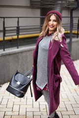 An autumn-winter lifestyle fashion portrait of a young stylish hipster woman in a red coat, waving...