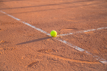 Tennis ball lying on white line on tennis court on sunny day.