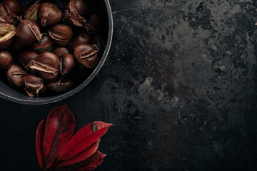 Pile of sweet roasted chestnuts on dark black rustic background. Traditional Christmas snack. Top...