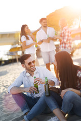 Happy couple smiling and drinking beer at beach